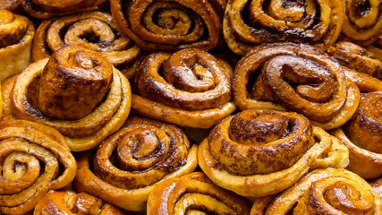 Close up image of freshly  handmade cinnamon swirls in natural light. With glistening glazed tops. A collection, each, individual with variations in colours, shapes and textures. Abstract landscape