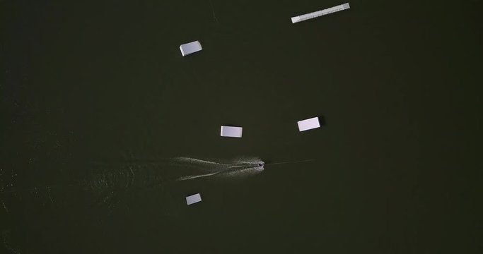 Aerial shot of a cableway in a lake with a wakeboarder making turns and tricks. Sportsman grinding and rotating on a funbox. Girl wakeboarding in wake park. Sport time summer concept.