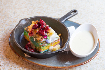 Rainbow Cake Slice with with vanilla sauce in a cafe. Cake in cast iron plate