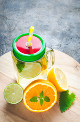 Jar of lemonade made of lemon, lime, orange and mint with a closed lid and a tube in it against background concrete floor.