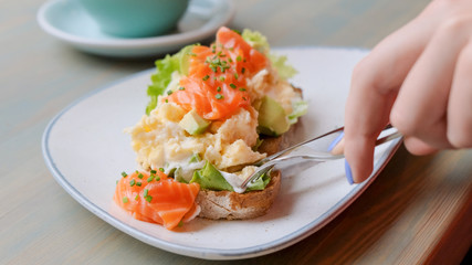 Close Up of female hands cutting avocado toast with salmon and egg While having breakfast 