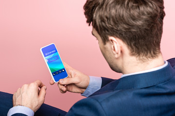 cropped view of businessman using smartphone with booking app, isolated on pink