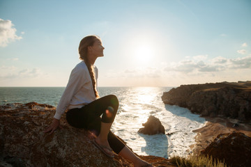 A young girl sitting on a rock on the background of the sea coast