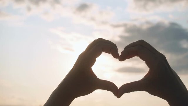 Beautiful Woman making heart shape with hands at sunset