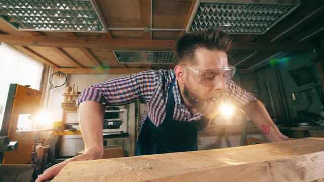 Joiner blows away wooden shavings from a table. Carpenter working.