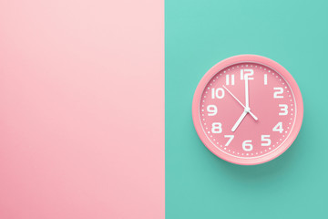 Fototapeta na wymiar Pink alarm clock on a colored background divided vertically into a pink and green half with copy space
