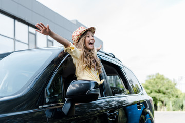 happy kid in straw hat with outstretched hands in car window