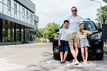 happy father in sunglasses standing near car with kids