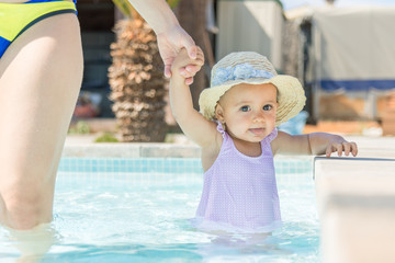 Baby girl with hat in swimming pool with her mother