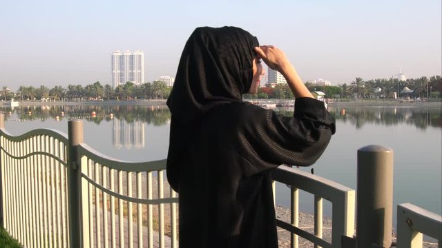 Muslim Arabic woman stares at the water on Barsha park in Dubai,UAE.