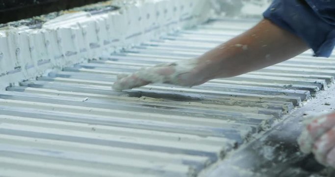 The man corrects defects of shape after the press machine. Creation of a construction panel element from plaster. Technological line for production of gypsum boards. Construction concept.