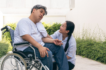 The wife is taking care of the husband sitting on wheelchair,  who is suffering from neurological diseases, or hemiplegia having a facial palsy and kinking fingers, to health and paralysis concept. - obrazy, fototapety, plakaty
