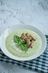 Cream soup of mashed potatoes with zucchini and basil and crackers on a dark background.