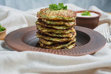 Zucchini fritters, vegetarian zucchini pancakes, served with fresh herbs and sour cream, top view. Light background.
