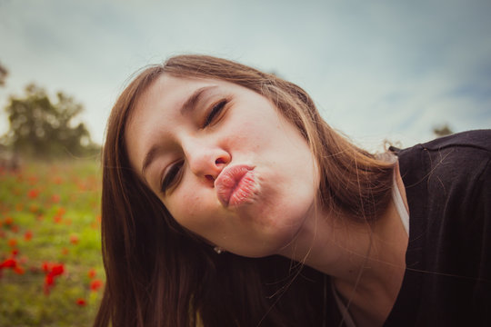 Young woman making duckface kiss while taking selfie picture with her smartphone or camera in field of red poppies