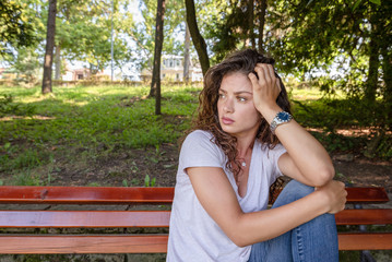 Young girl or woman sitting alone on the park bench feeling depressed and sad after she had argue and fight with her boyfriend or husband and she thinking about her life with sadness on her face