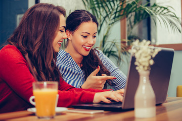Two female friends using laptop and drinking coffee together