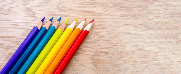 Fototapeta premium Different colored pencils photo with space for text. Seven pencils of rainbow colors lie on the table. Copyspace. Back to school. Wooden background.