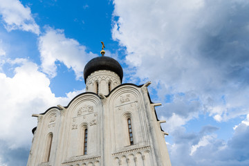 Fototapeta premium Orthodox church on a green meadow with trees and blue cloudy sky