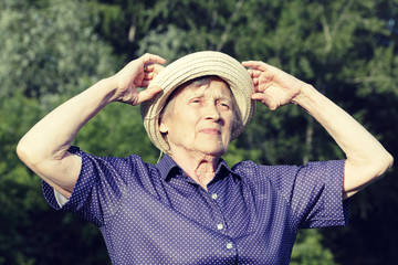 A portrait of an old woman in park who straightens her hat. Sunny day.
