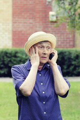 Portrait of an elderly woman in hat with a phone in her hand. Senior experiences different emotions in the communication process.