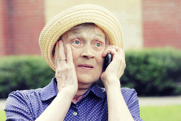 Portrait of an elderly woman in hat with a phone in her hand. Senior experiences different emotions in the communication process.