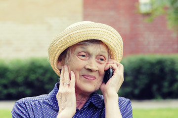Portrait of an elderly woman in hat with a phone in her hand. Senior experiences different emotions in the communication process.