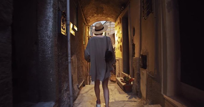 Excited pretty girl walks in tight street in old vintage town at daytime. Female tourist exploring new places in coastal town Rio Majore. Summer tour to Italy.