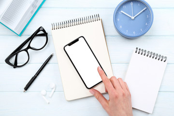 Smartphone with notepads, glasses and round clock on wooden background