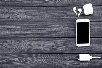 Smartphone with earphones and charger on wooden background