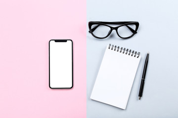 Smartphone with notepad and glasses on colorful background