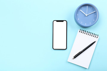 Smartphone with notepad and round clock on blue background