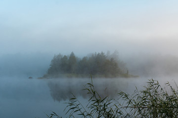 Fototapeta premium Morning landscape on the lake. The fog is moving in calm water. Misty morning in the forest. Mystical atmosphere