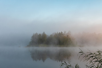 Morning landscape on the lake. The fog is moving in calm water. Misty morning in the forest. Mystical atmosphere