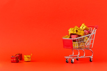 Shopping cart full of gifts on red background.  Close-up of shopping trolley on with some copy space. Consumer concept. The concept of buying gifts for the holidays. 