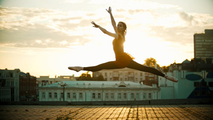 Young woman ballerina jump performing a split - bright sunset