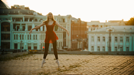 Young smiling woman ballerina training on the roof - standing on her tiptoes