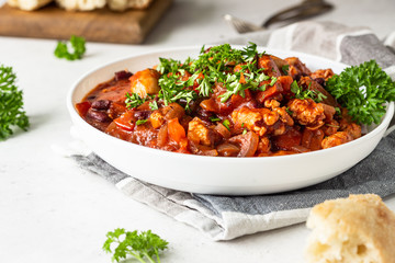 Meat stew with red beans, bell pepper and onion in tomato sauce in a white plate over light grey slate or stone background. 