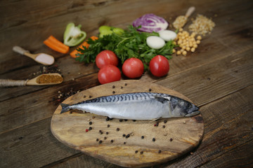 Fresh mackerel isolated on a wooden cutting board with vegetables, sprouted beans and herbs and spices on a wooden table. Healthy food. Mediterranean diet.