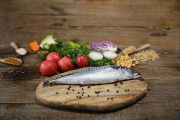 Fresh mackerel isolated on a wooden cutting board with vegetables, sprouted beans and herbs and spices on a wooden table. Healthy food. Mediterranean diet. With space for text. 