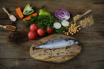 Fresh mackerel isolated on a wooden cutting board with vegetables, sprouted beans and herbs and spices on a wooden table. Healthy food. Mediterranean diet.