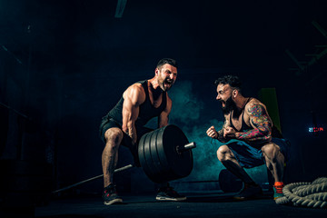 Fototapeta Two muscular bearded tattoed athletes training, one lift heavy weight bar when other is motivating. Scream. Working hard. Exercise for the muscles of the back obraz