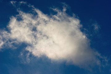 Naklejka na ściany i meble Sunlit white cloud against the background of dark blue sky. Fresh atmosphere, natural light