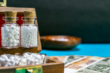 Homeopathic medicine glass bottles of pills in wooden box on Indian currency and blue surface with blurred wood spoon and dark background - Savings with Homeopathic Medicine concept