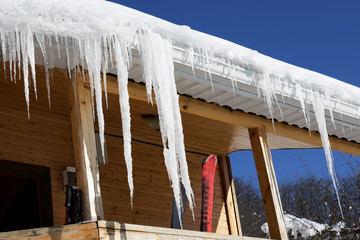 Wooden house with snow cornice and icicles on roof and ski equipment