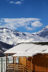 Wooden house with snowy roof and icicles at snow winter mountains