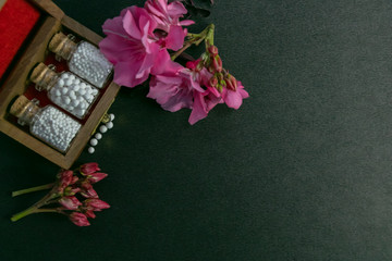 Natural homeopathy - Top view of homeopathy medicine bottles in wooden old box with pink flowers and some scattered globules on dark background © winistudios
