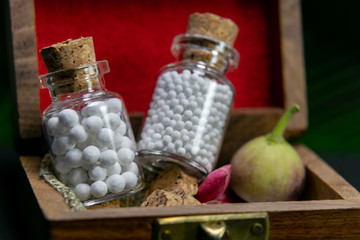 Natural medicine concept - Homeopathic pills in vintage glass bottles in wooden old box with flower petal and wild fruit on dark background