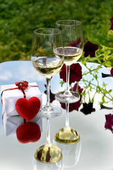 glasses of white wine, a gift and a heart-shaped box and also flowers.