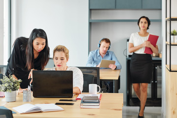 Group of young business people sitting at their workplaces and working with laptop computers with young businesswoman walking along the office corridor